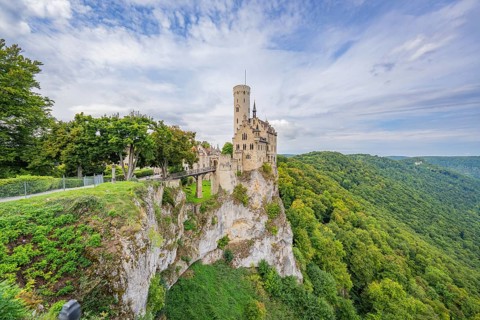 Impressive castle stands on a lush cliff, surrounded by mountains and sky, Lichtenstein Castle,