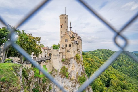 Castle on a hill, framed by green forest and viewed through a lattice, Lichtenstein Castle,