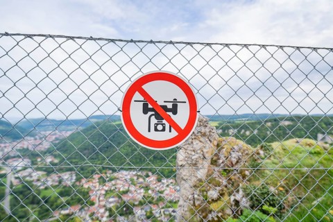 Lattice fence with drone prohibition sign in front of a wide panoramic view over the landscape,