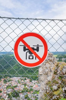 Sign on the fence indicating a drone ban, with a view of the landscape below, Lichtenstein Castle,