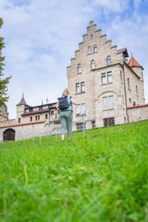 A woman walks up a grassy hill towards an imposing historic castle, Lichtenstein Castle,
