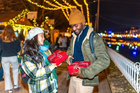 Young multiethnic couple exchanging christmas gifts at a christmas market, enjoying winter holidays