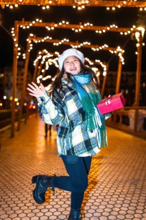 Happy young woman holding a christmas gift, reveling in the enchanting glow of festive lights and