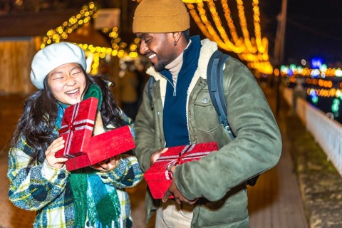 Young multiethnic couple exchanging christmas gifts at a christmas market, enjoying the festive