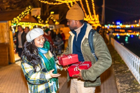 Happy multiethnic couple exchanging christmas gifts at a christmas market, enjoying winter holidays