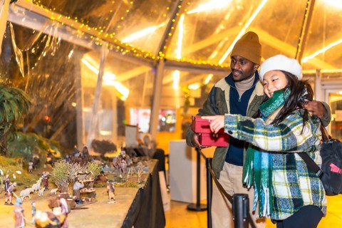 Happy multiethnic couple holding christmas gifts and enjoying a nativity scene exhibition