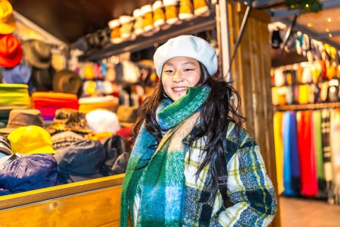 Young woman wearing a beret and scarf, smiling at a christmas market stall selling winter clothes
