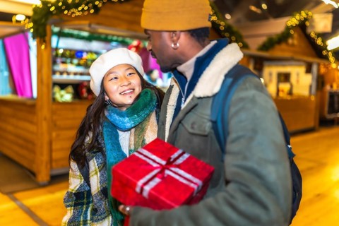 Young multiethnic couple holding a christmas gift, enjoying christmastime at a christmas market