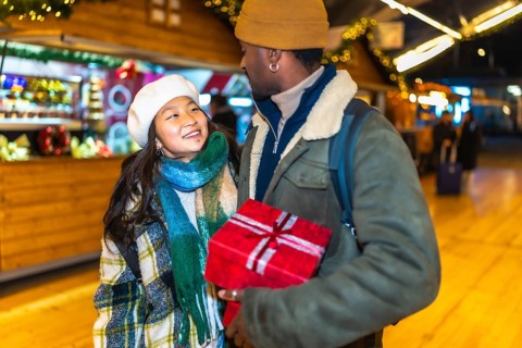 Young multiethnic couple joyfully holding a beautifully wrapped christmas gift while enjoying the