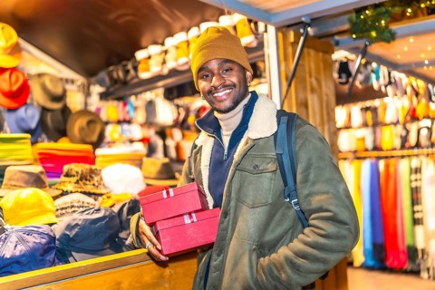 Young man holding christmas presents at a christmas market stall, enjoying the festive atmosphere