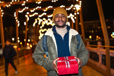 Young man holding christmas gift while walking on a city bridge decorated with christmas lights