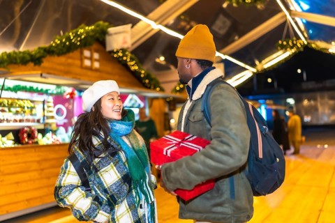 Young multiethnic couple exchanging christmas gifts at a christmas market, enjoying the festive
