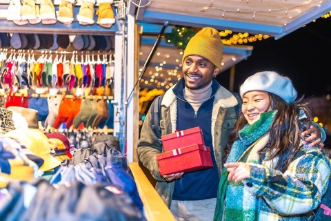 Young multiethnic couple enjoying christmas shopping at a decorated christmas market, holding red