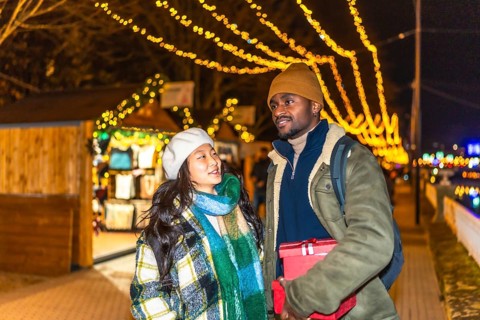 Young multiethnic couple walking and enjoying christmastime at a decorated outdoor market with