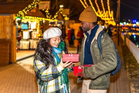 Happy multiethnic couple exchanging christmas gifts at a festively decorated christmas market,