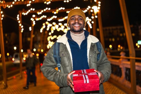 Smiling tourist holding christmas present while enjoying winter holidays in decorated city