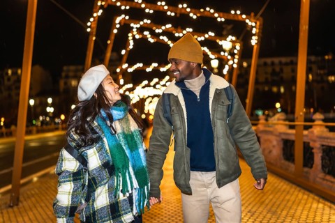 Young multiethnic tourists couple holding hands, enjoying christmas lights decoration at night