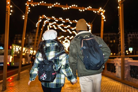 Multiethnic couple walking on bridge at night, holding hands and enjoying christmas lights
