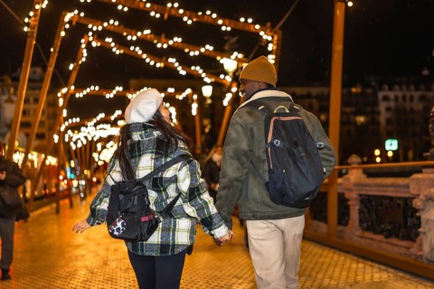 Young multiethnic couple walking on bridge with christmas lights, enjoying winter holidays