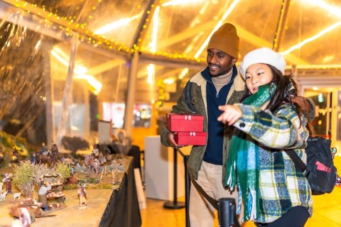 Happy multiethnic couple holding christmas gifts and admiring a nativity scene at a christmas