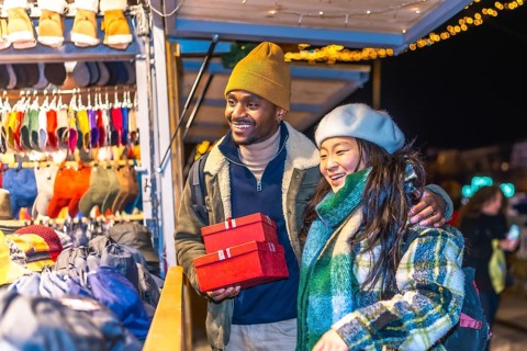 Multiethnic couple enjoying christmas shopping at a decorated christmas market, holding red gift
