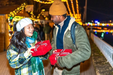 Young multiethnic couple exchanging christmas gifts at a christmas market, enjoying the festive