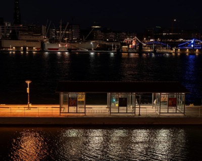 Night shot of a pontoon with bus shelter at the theatre on the Elbe with a view of the lighting of