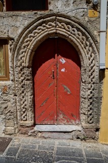 Red door with Romanesque arch and decorative stone carvings in an old façade, Turkish Quarter,