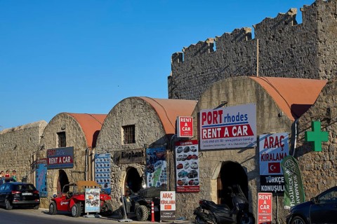 Outside the fortress walls, warehouses, row of buildings with car hire signs under historic stone