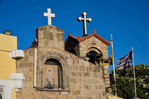 Church of Agios Panteleimon, stone church with crosses and flags in the background under a blue