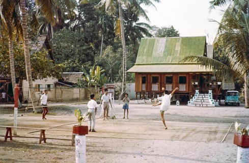 Traditional village houses in coconut palm trees, boys and young men playing Sepak Takraw foot