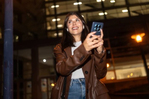Young woman happily smiling and looking up while using her smartphone and wireless earbuds at