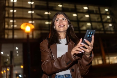 Young woman smiling and looking up, listening to music with wireless earbuds and using a smartphone