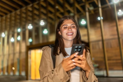 Young woman in a trench coat smiling, checking her smartphone, and experiencing happy moments while