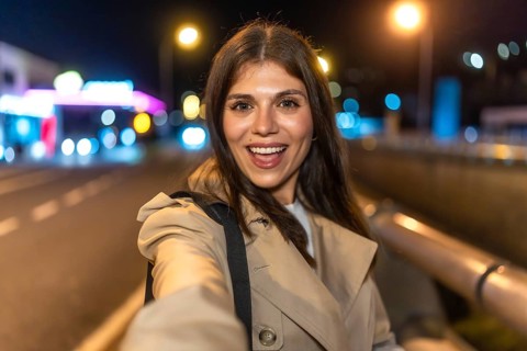 Young woman smiling and taking a selfie on a lively city night, bokeh street lights and light