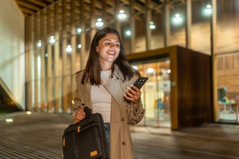 Young businesswoman smiling while checking her smartphone, holding a briefcase and walking alone on