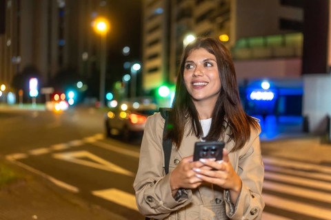 Young woman smiling and looking away while using a mobile phone on a pedestrian crossing, waiting