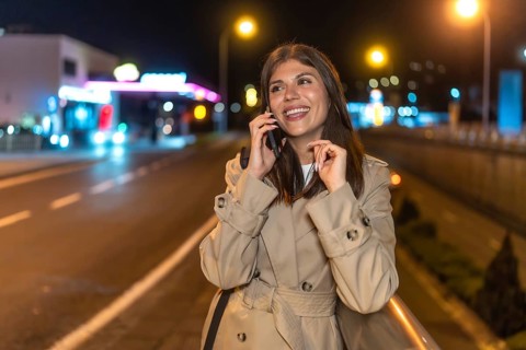 Young woman smiling and communicating on a smartphone, walking along a vibrant urban street during