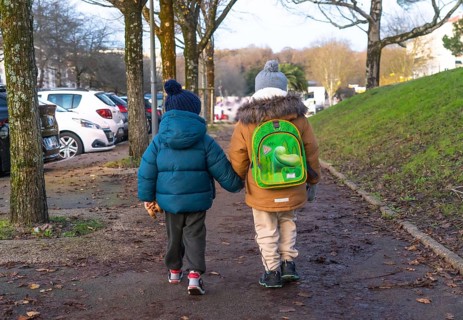 Two young children holding hands and walking home from school on a chilly winter day in bayonne,