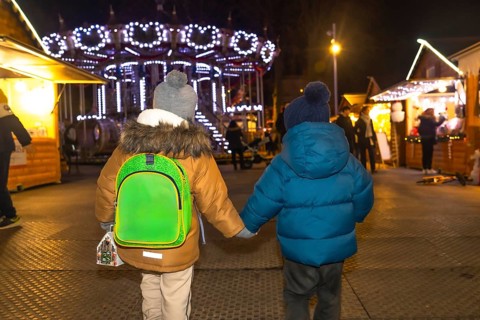 Two young boys holding hands are walking through a christmas market at night in bayonne, france,