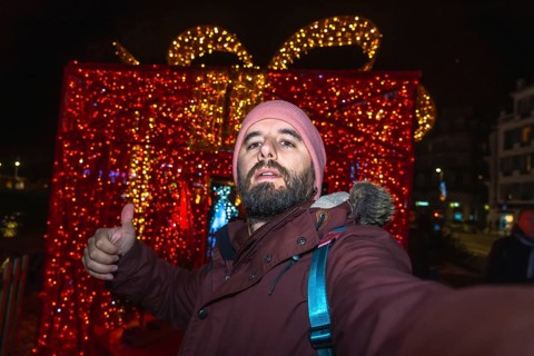 Tourist taking a selfie and making thumbs up sign with christmas lights and decorations in bayonne,