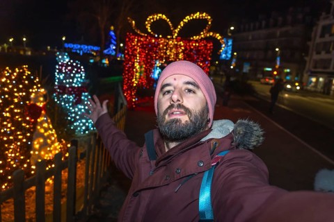 Bearded tourist taking a selfie with christmas lights and decorations in bayonne, france, at night
