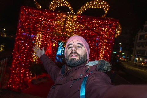 Bearded man taking a selfie in front of giant luminous christmas gift box in bayonne, france