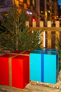 Large red and blue christmas presents sit on a wooden platform, adorned with fir branches, creating