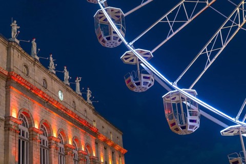 Ferris wheel cabins rotating over bayonne city hall illuminated in orange during christmas night in
