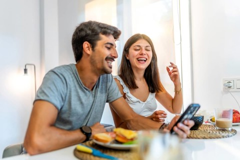 Young couple enjoying breakfast and having fun while using a smartphone in their modern kitchen