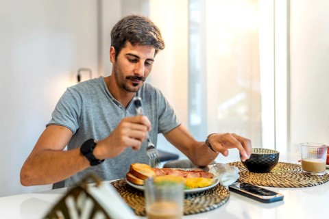 Young man enjoying breakfast with crispy bacon, fluffy eggs, toast, and steaming coffee in a