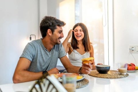 Young couple enjoying breakfast at home, laughing and sharing joyful moments together, creating a
