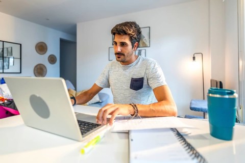 Young male freelancer concentrating on his laptop, working remotely from his modern home office