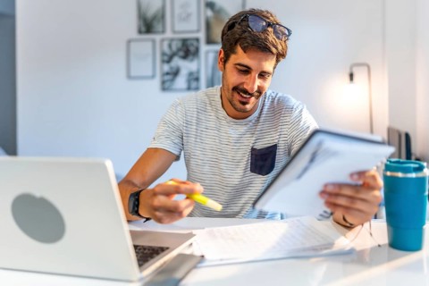 Young male freelancer comparing information on his tablet with data on his laptop, working from his